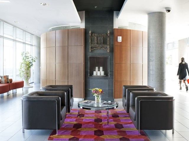 Modern lounge with black chairs, a colorful rug, and a fireplace in a bright lobby.