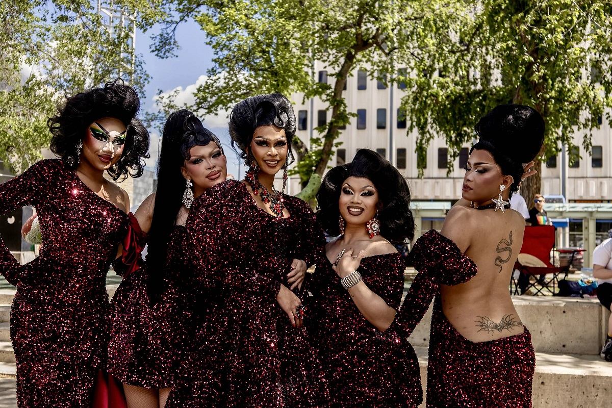 Group in matching red sequined outfits posing outdoors with dramatic hairstyles and accessories.