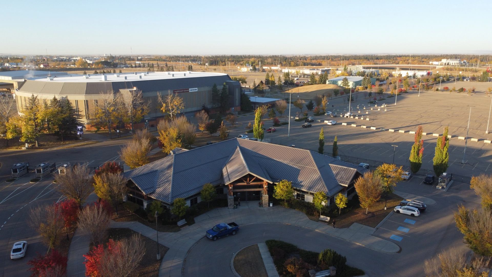 Aerial view of a rustic lodge building and a large sports arena, surrounded by autumn trees and vast parking lots.