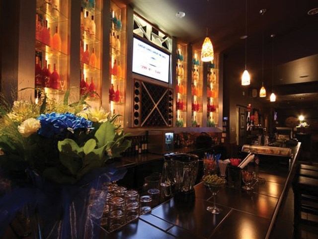 Stylish bar with glowing shelves, pendant lights, and floral decor.