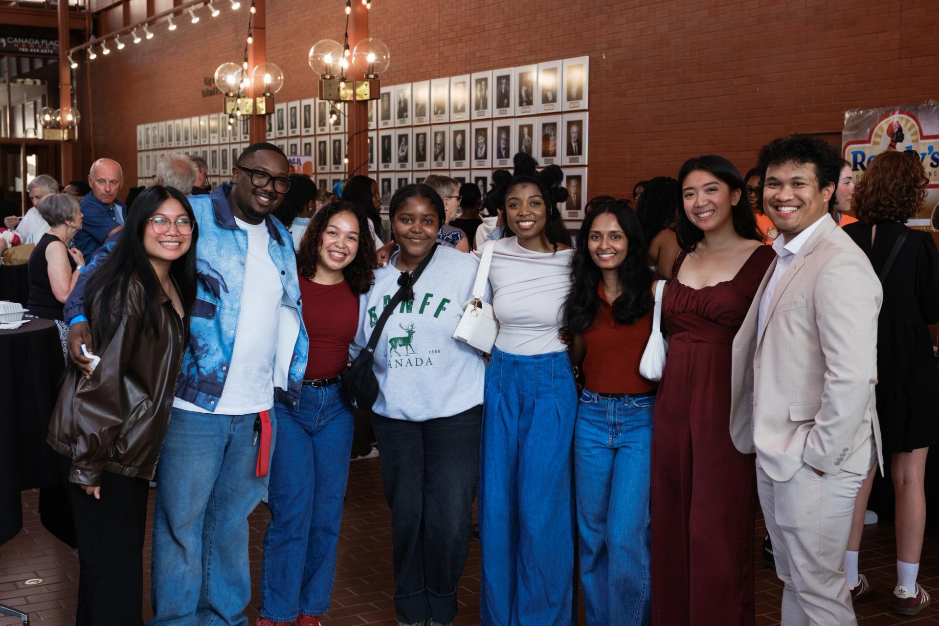 Group of people posing together at an indoor event with photo wall behind them.