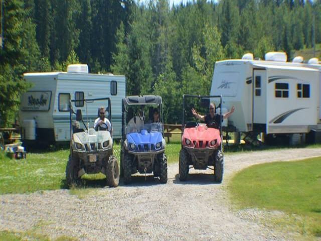 Three ATVs and RVs parked in forested campground with people enjoying the outdoors.