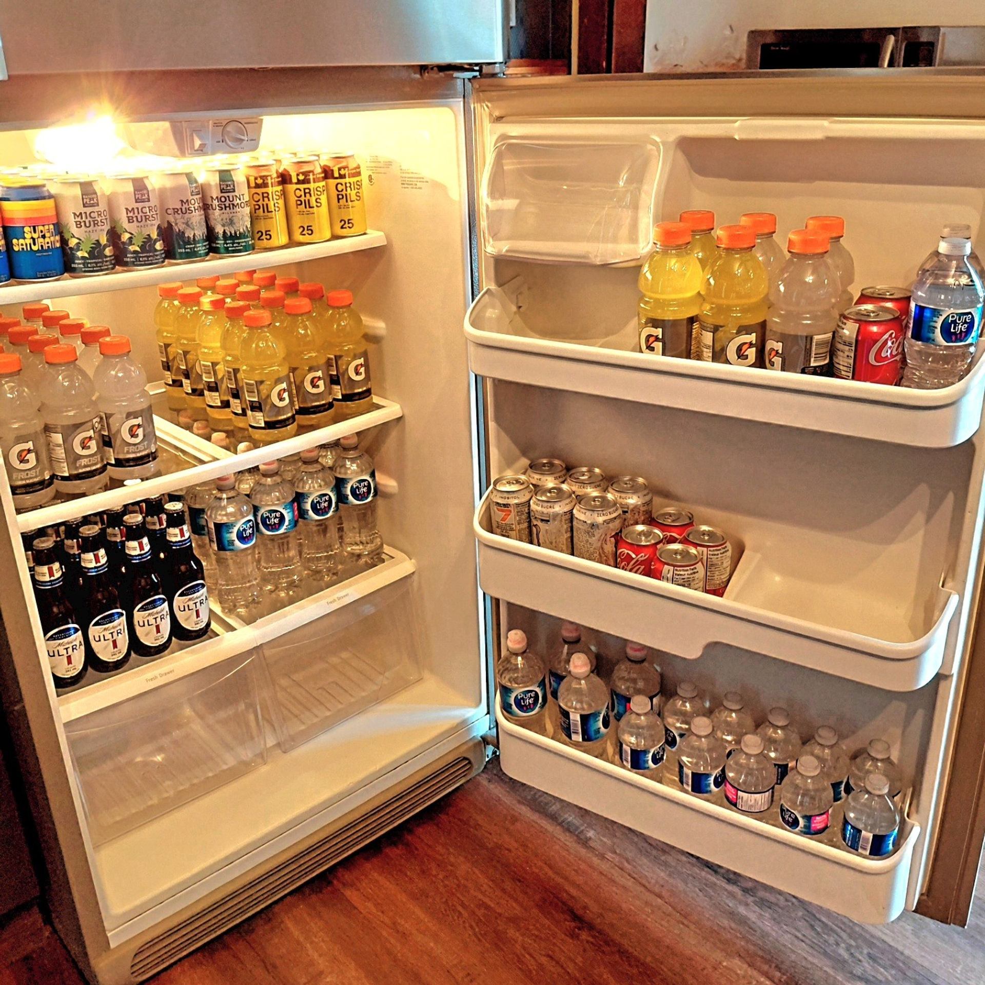 Open refrigerator filled with assorted canned beer, sports drinks, soft drinks and bottled water.