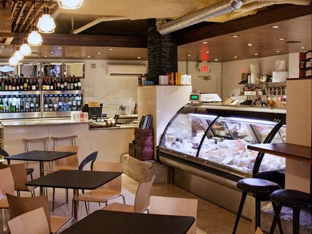 Cozy café interior with tables, display case, and shelves stocked with bottles.