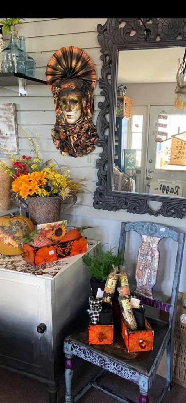 Antique mirror and decorative face sculpture with flowers and gift boxes in a shop display.