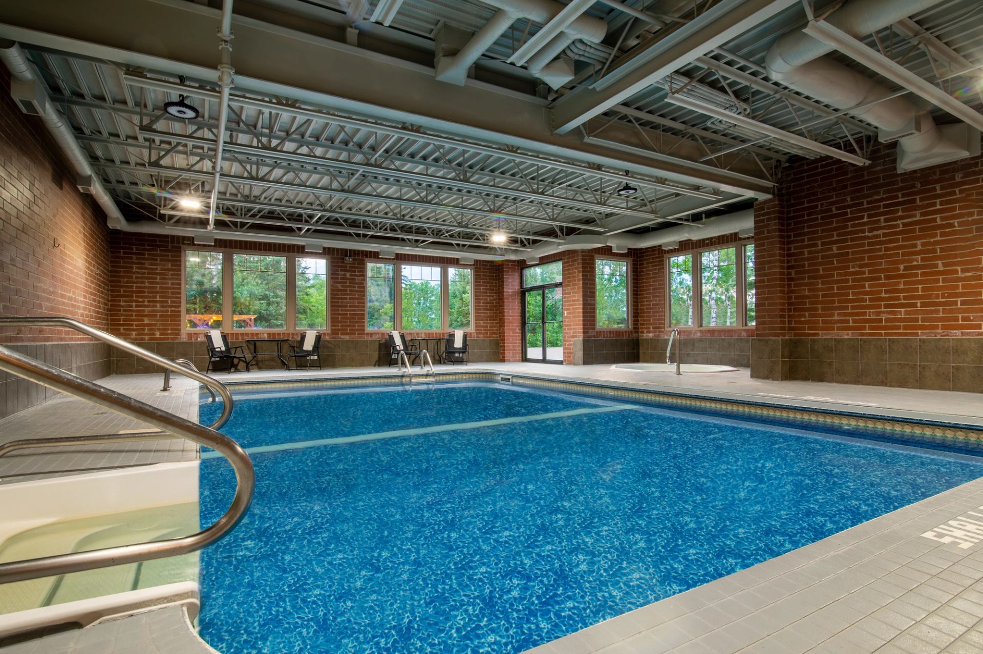 Indoor pool area with bright blue water, brick walls, and large windows letting in natural light.