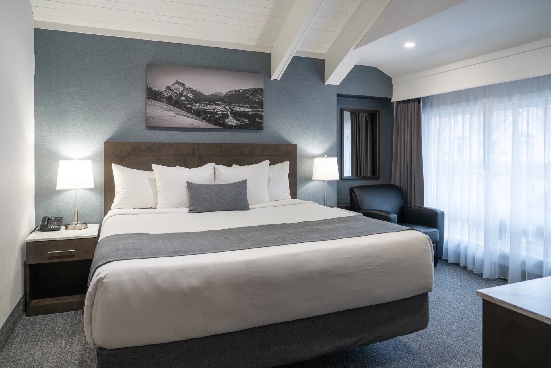 Modern hotel room with large bed, mountain photo, and cozy lighting.