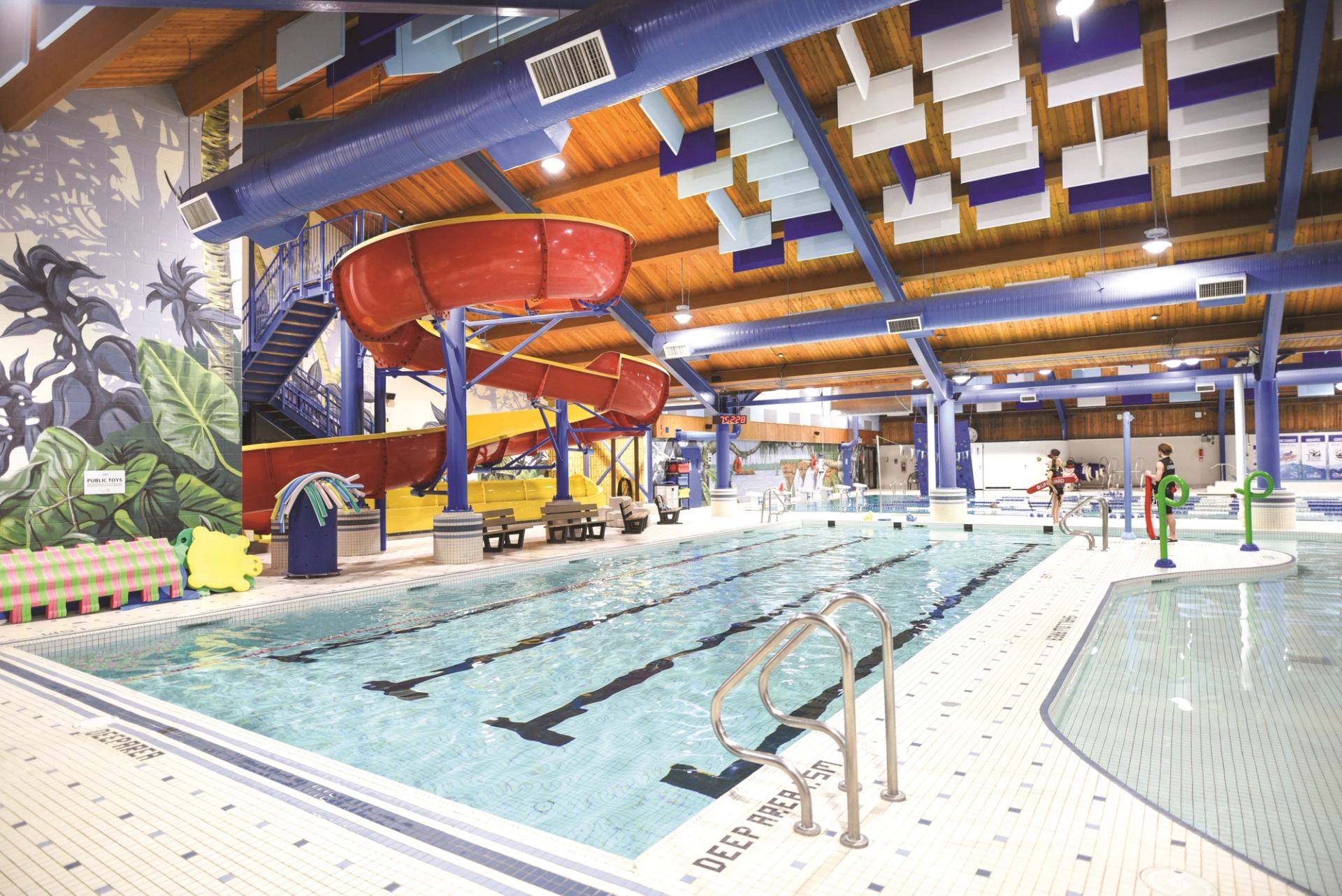 Indoor pool with swim lanes, red slide, and tropical-themed murals.