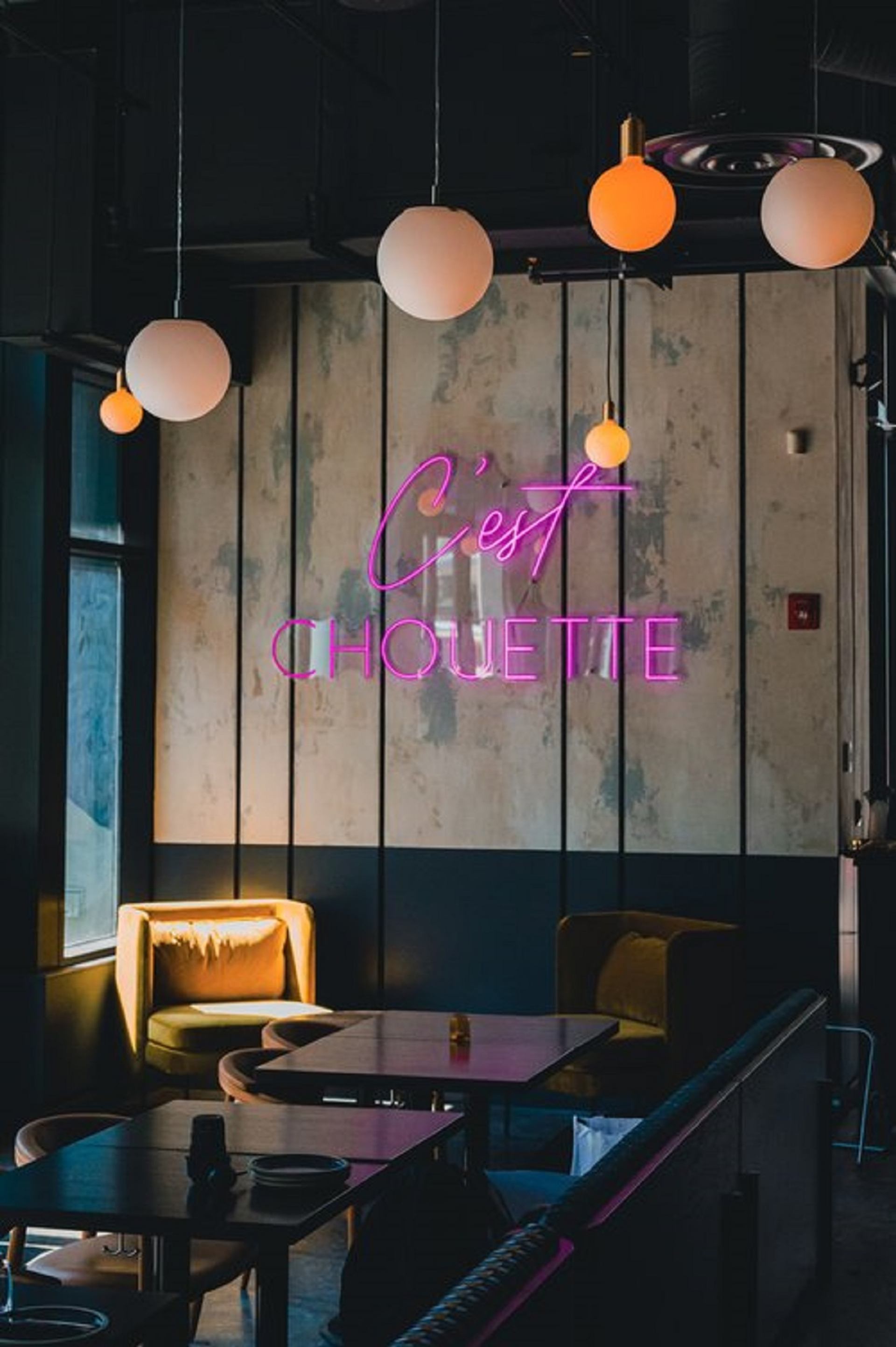 A neon sign on the interior wall that says "C'est Chouette", with comfortable chairs and tables.