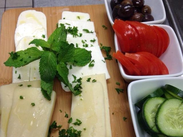 Sliced cheese, tomato, and cucumber with olives on a wooden serving board.
