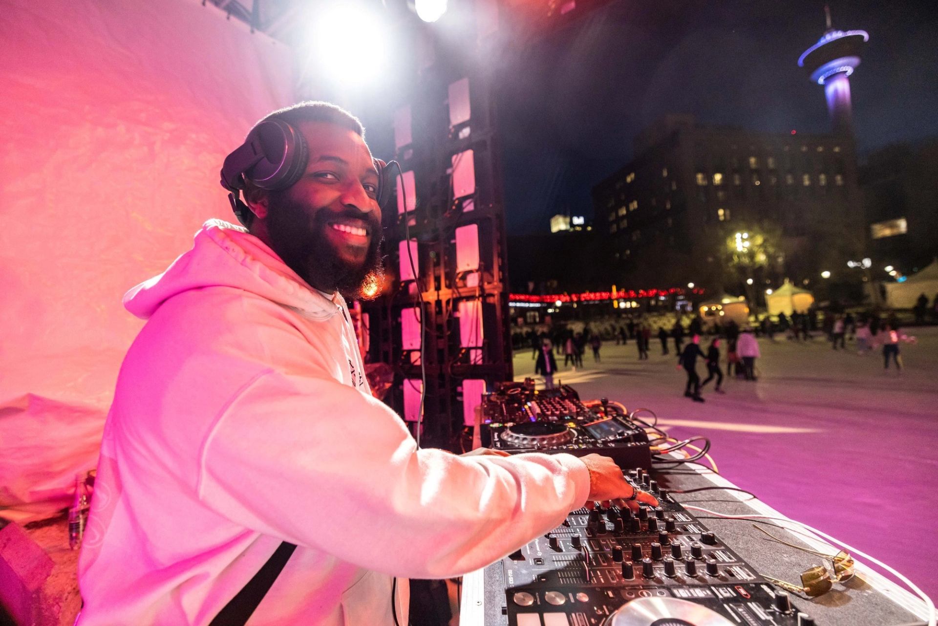 Smiling DJ at turntables beside outdoor skating rink.