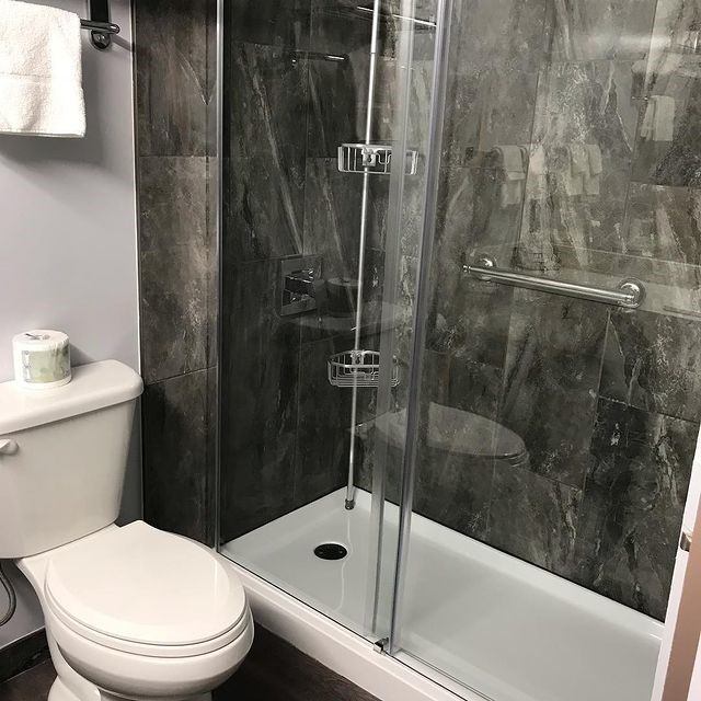 Modern bathroom with glass shower enclosure, gray tile walls, and white toilet.