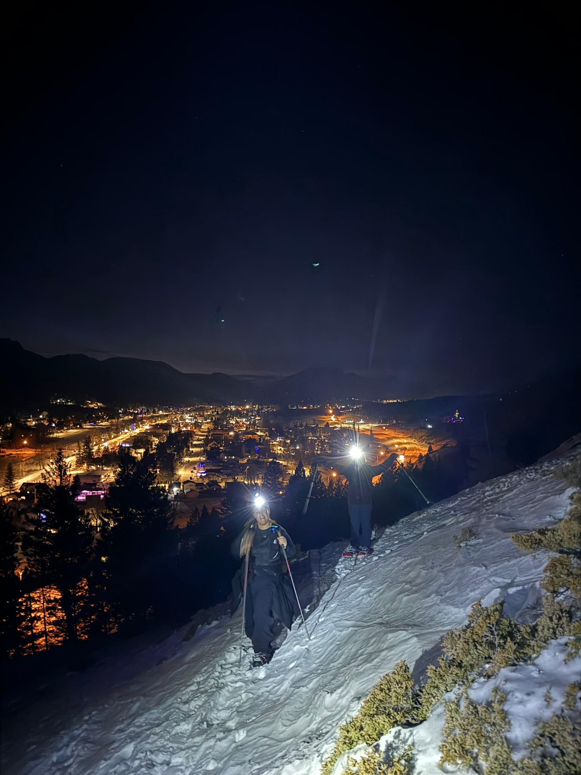 Snowshoeing under the stars with city lights and mountains in the background.