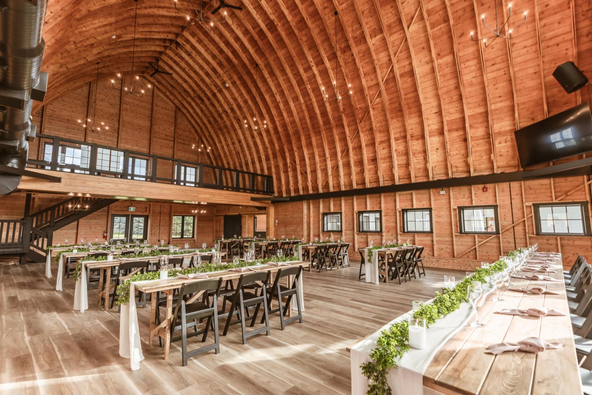 Rustic wooden event hall with long decorated tables, high arched ceiling, and soft natural lighting.