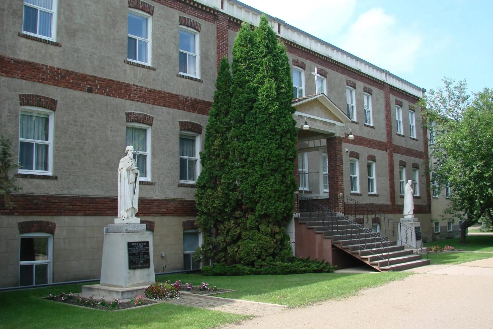 Brick building with entrance stairs and two statues in front on the museum grounds.
