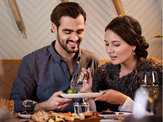 A couple sharing a meal, with the man offering a bite to the woman at a cozy dinner table.