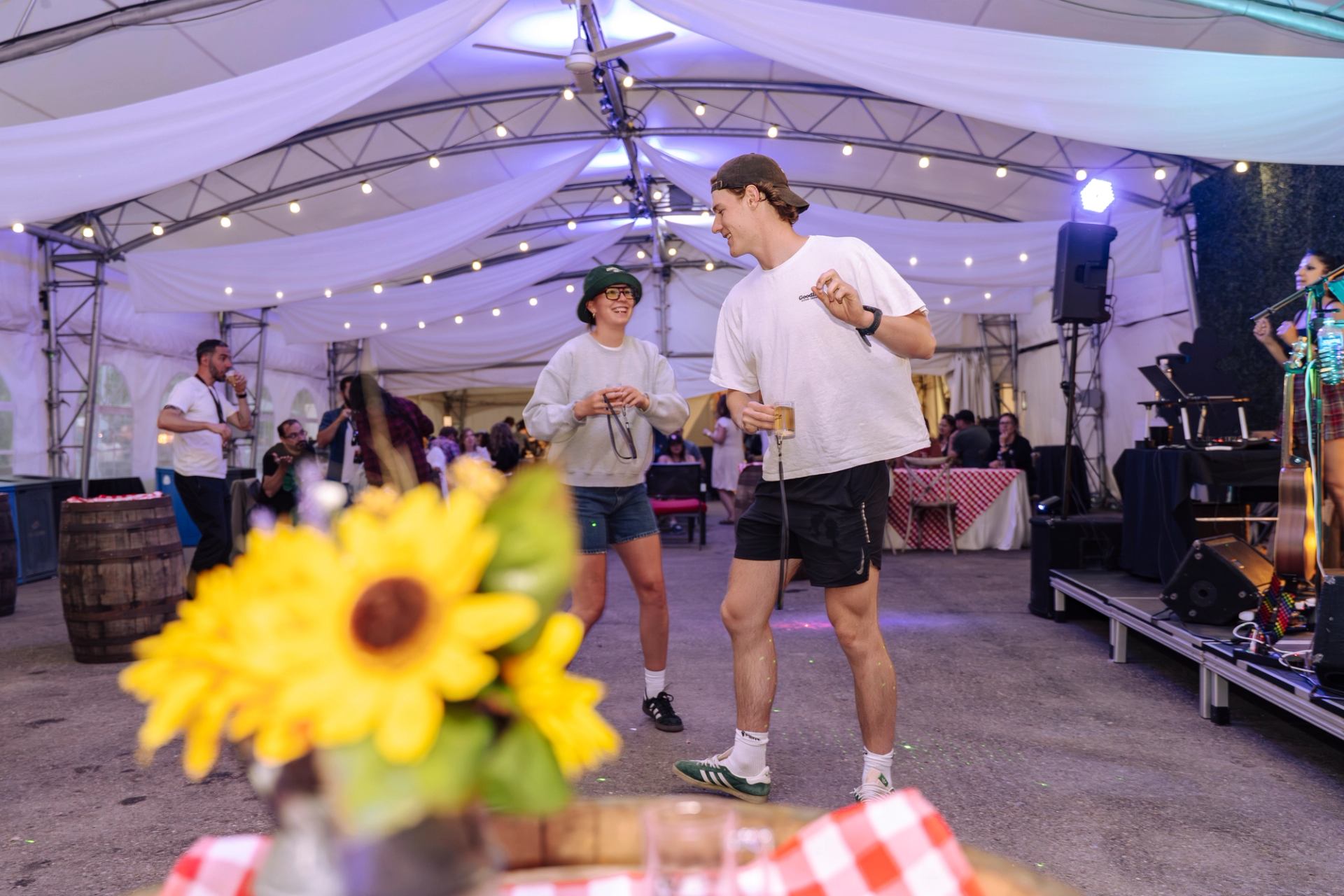 Guests dance with drinks under a lit tent near a live music stage.