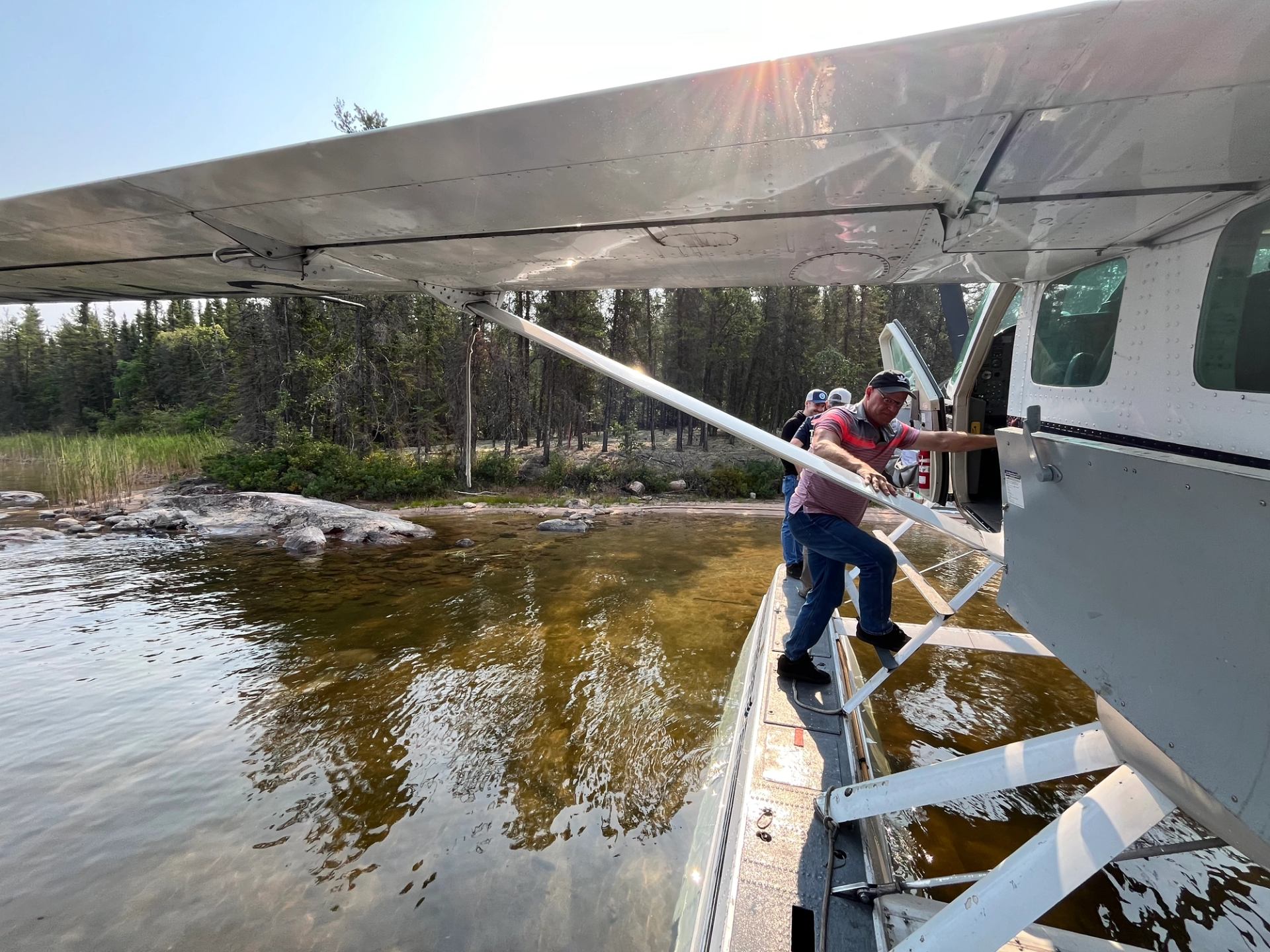 Person boarding seaplane on lake near forested shoreline.