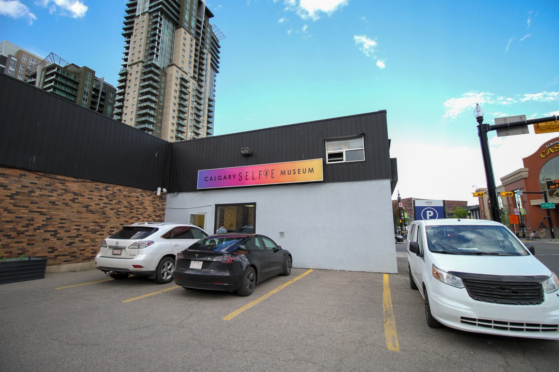 Calgary Selfie Museum exterior with parked cars in front and tall condos behind.