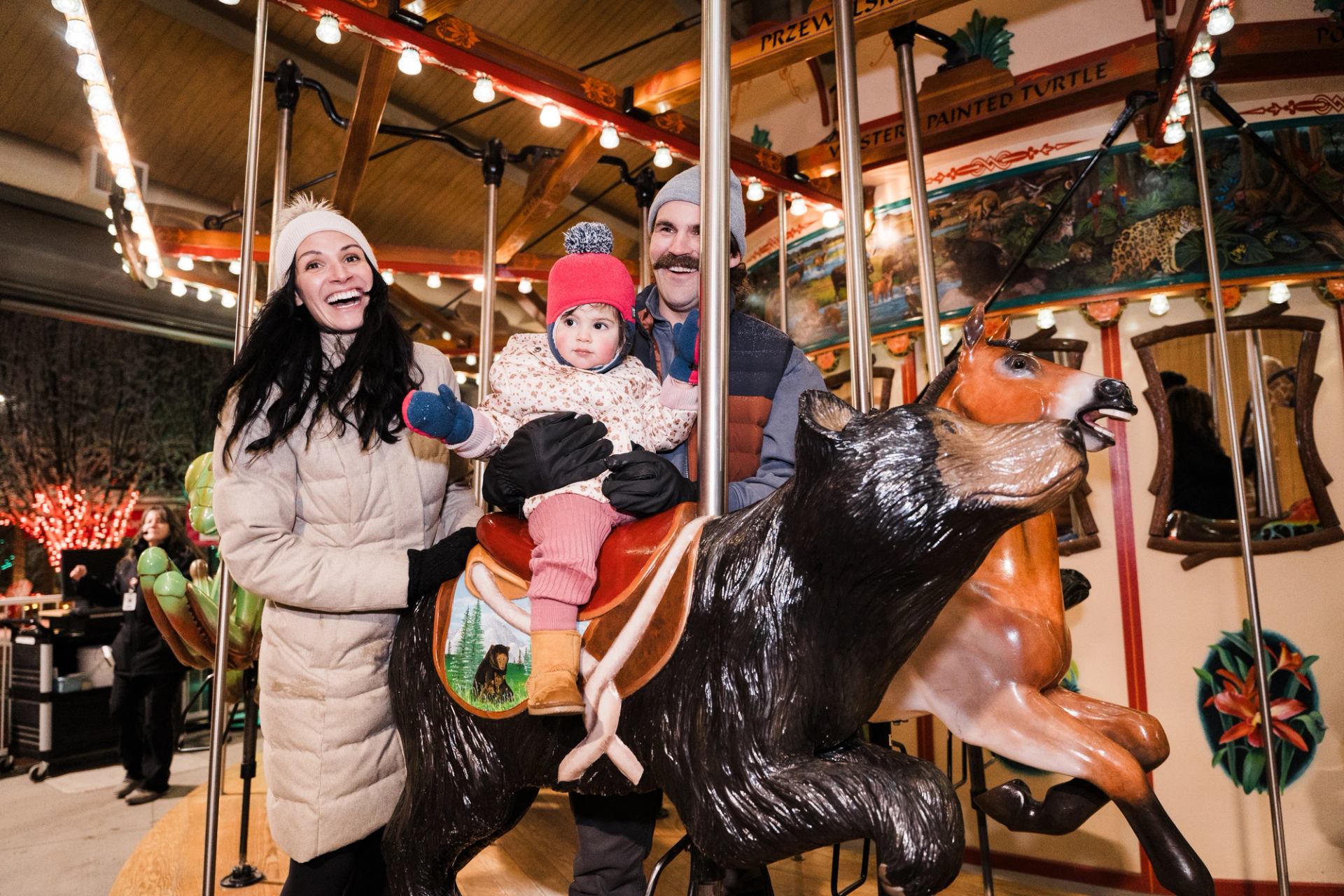 Family riding a carousel during ZooLights, surrounded by festive holiday lights.