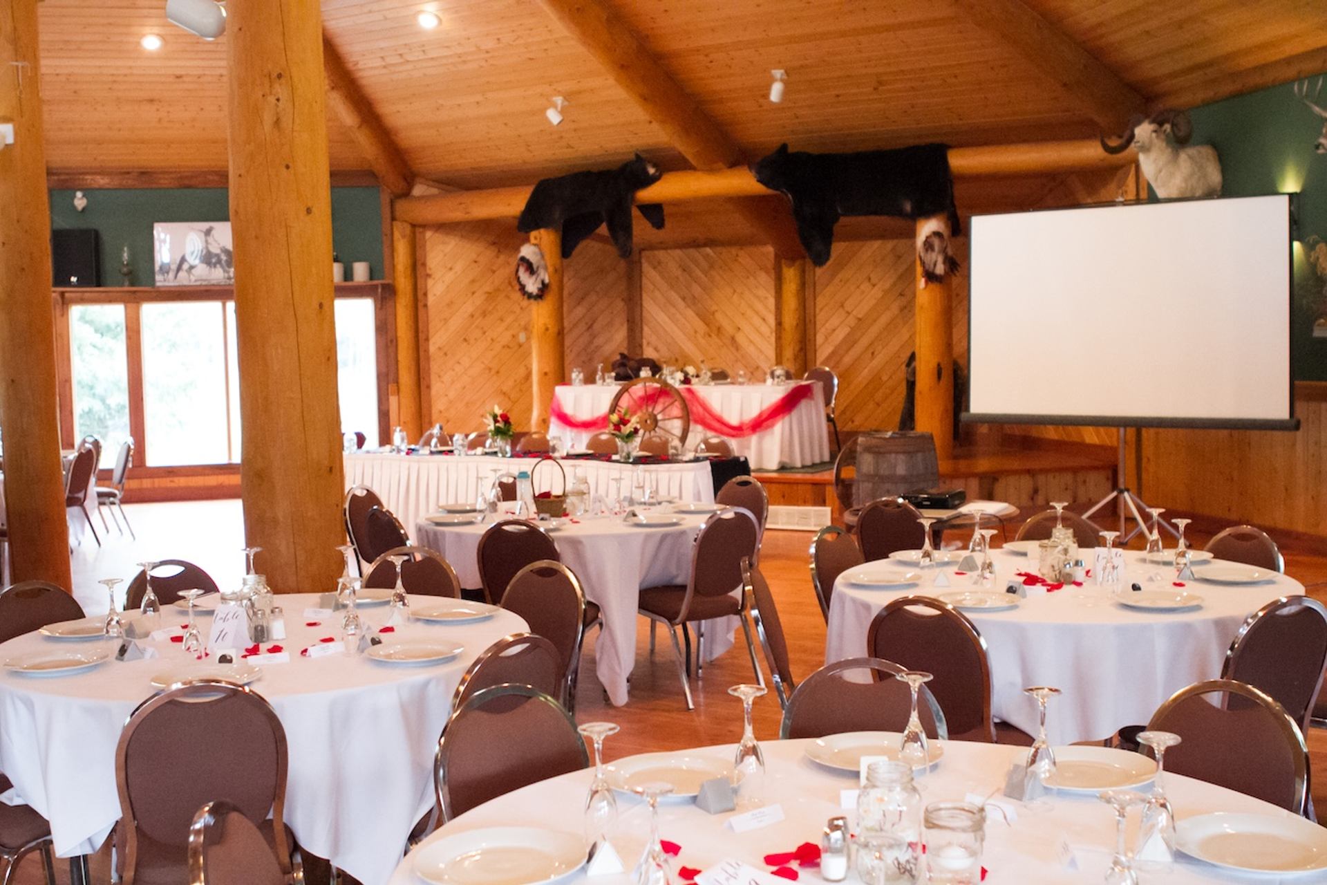 Reception room with round tables, wooden beams, and a decorated head table.