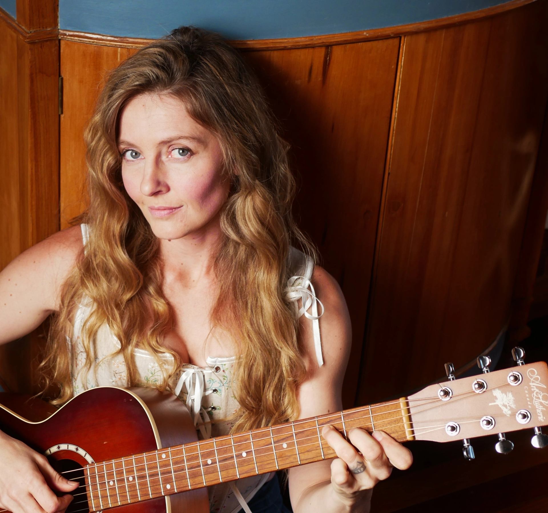 Person playing an acoustic guitar indoors against a wooden wall.