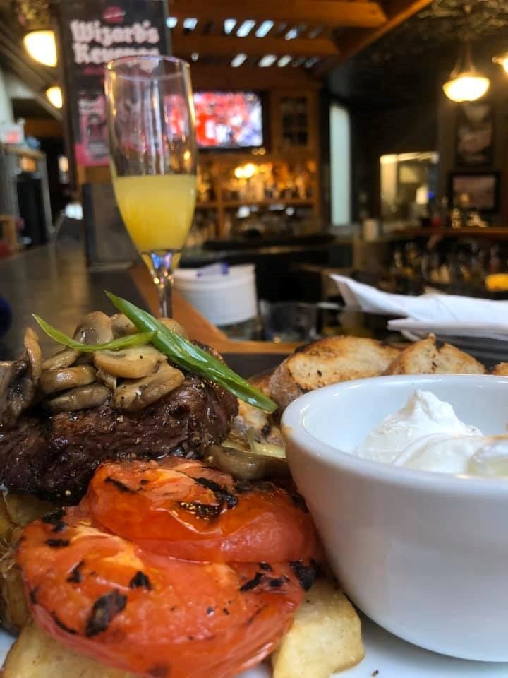 Close-up of a plated steak meal with grilled vegetables and a drink in a cozy pub setting.