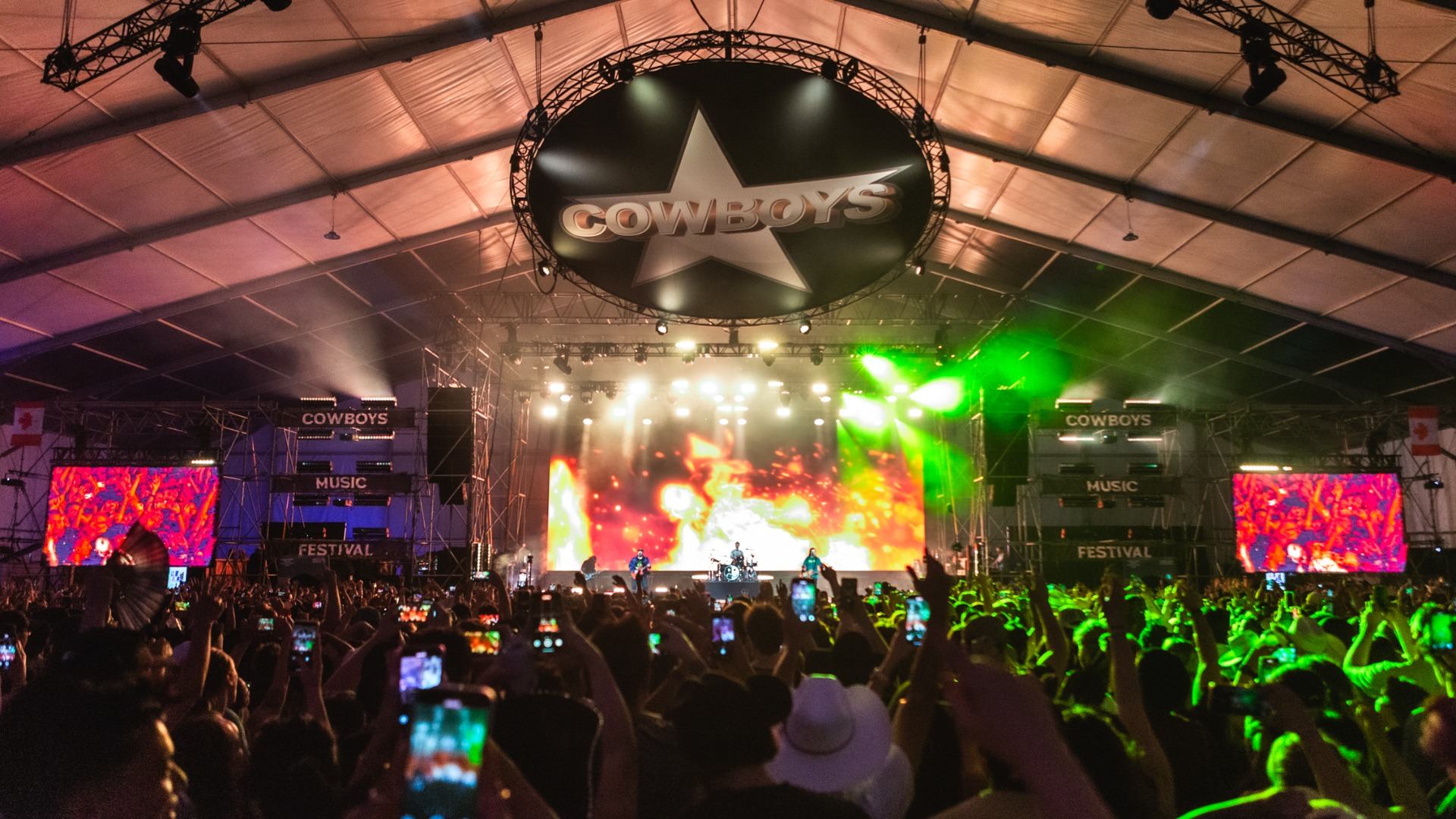 Large crowd watching a band perform on a bright, colorful stage at Cowboys Music Festival.