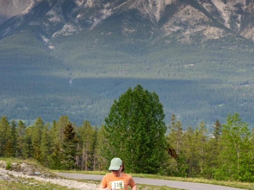 Runner in orange shirt on road with Rocky Mountain valley and trees in background.