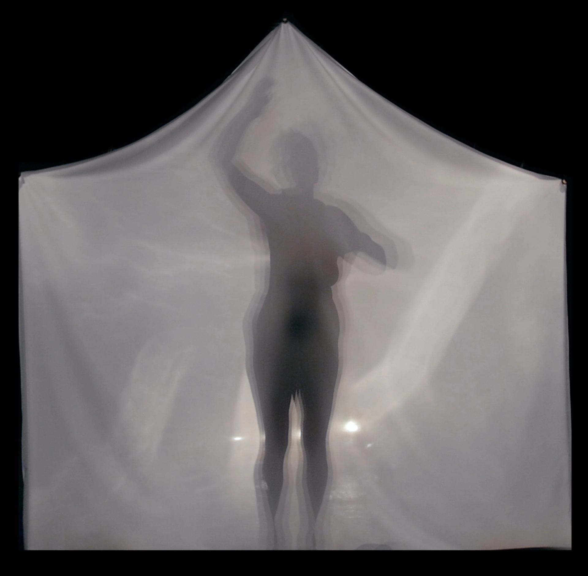 Motion-blurred silhouette of a person behind a translucent white tent-shaped fabric.