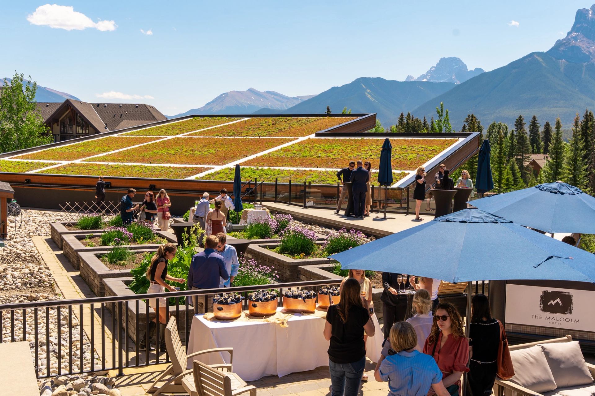 Outdoor gathering at The Malcolm Hotel rooftop garden with mountain views and blue umbrellas.