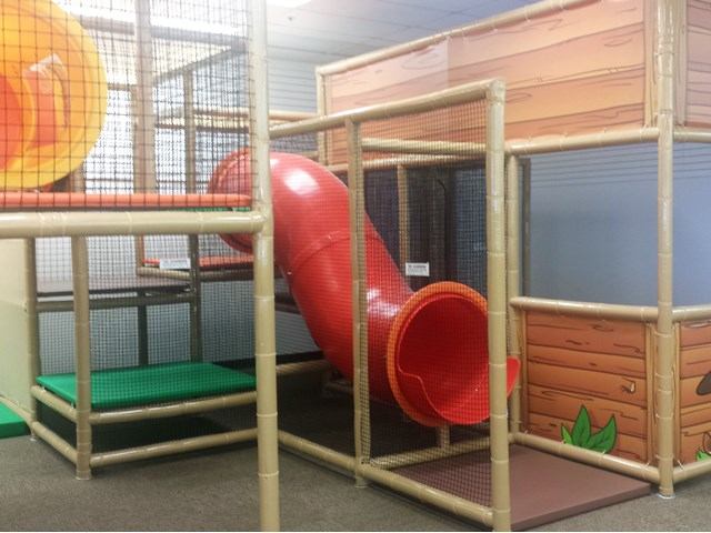 Indoor playground structure with red tube slide, climbing platforms and safety netting.