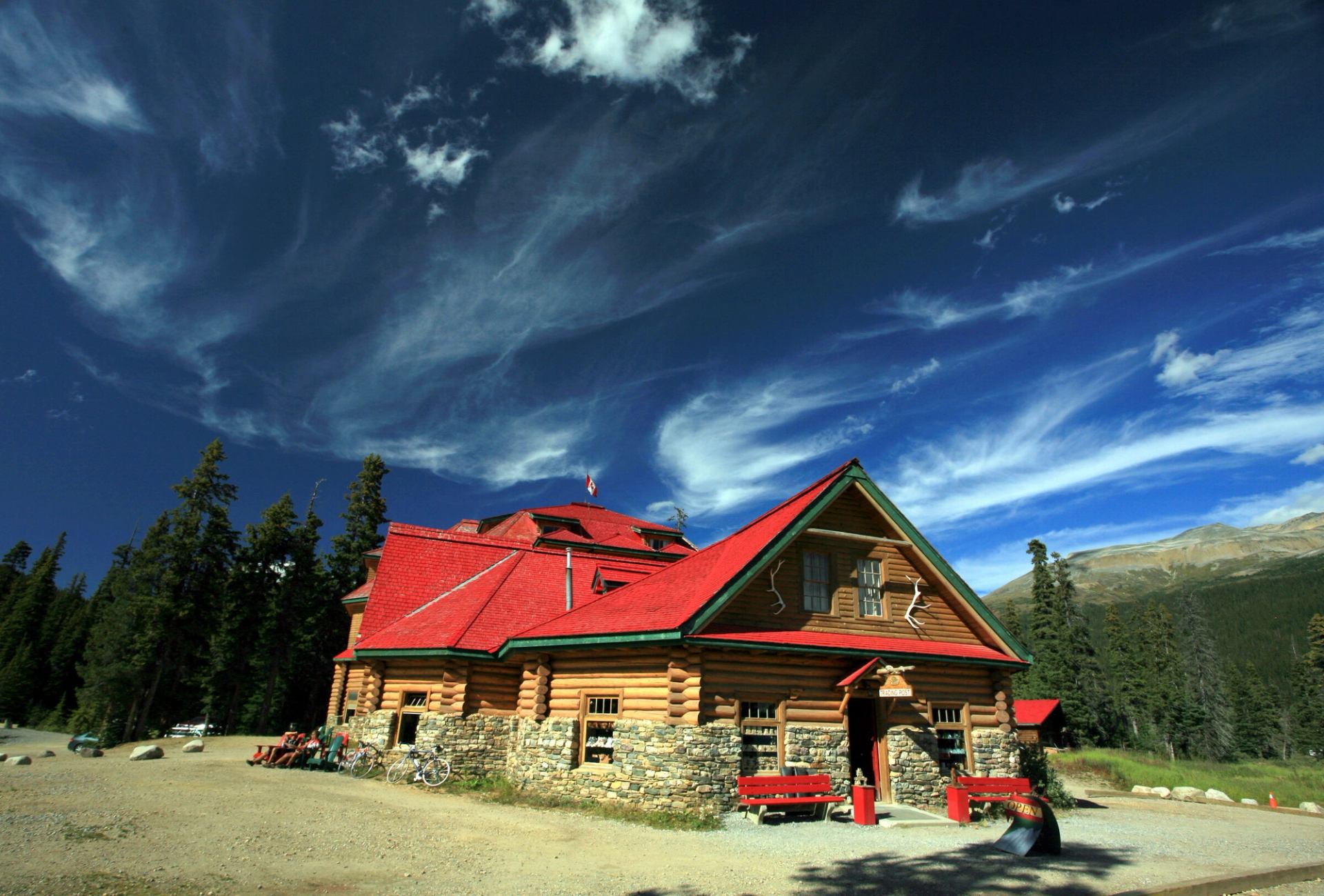 The lodge with a bright red roof and stone foundation stands under a vivid blue sky.