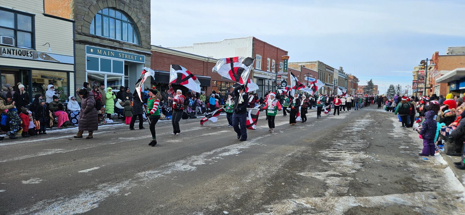 Parade participants march with red, white, and black flags down snowy Main Street.