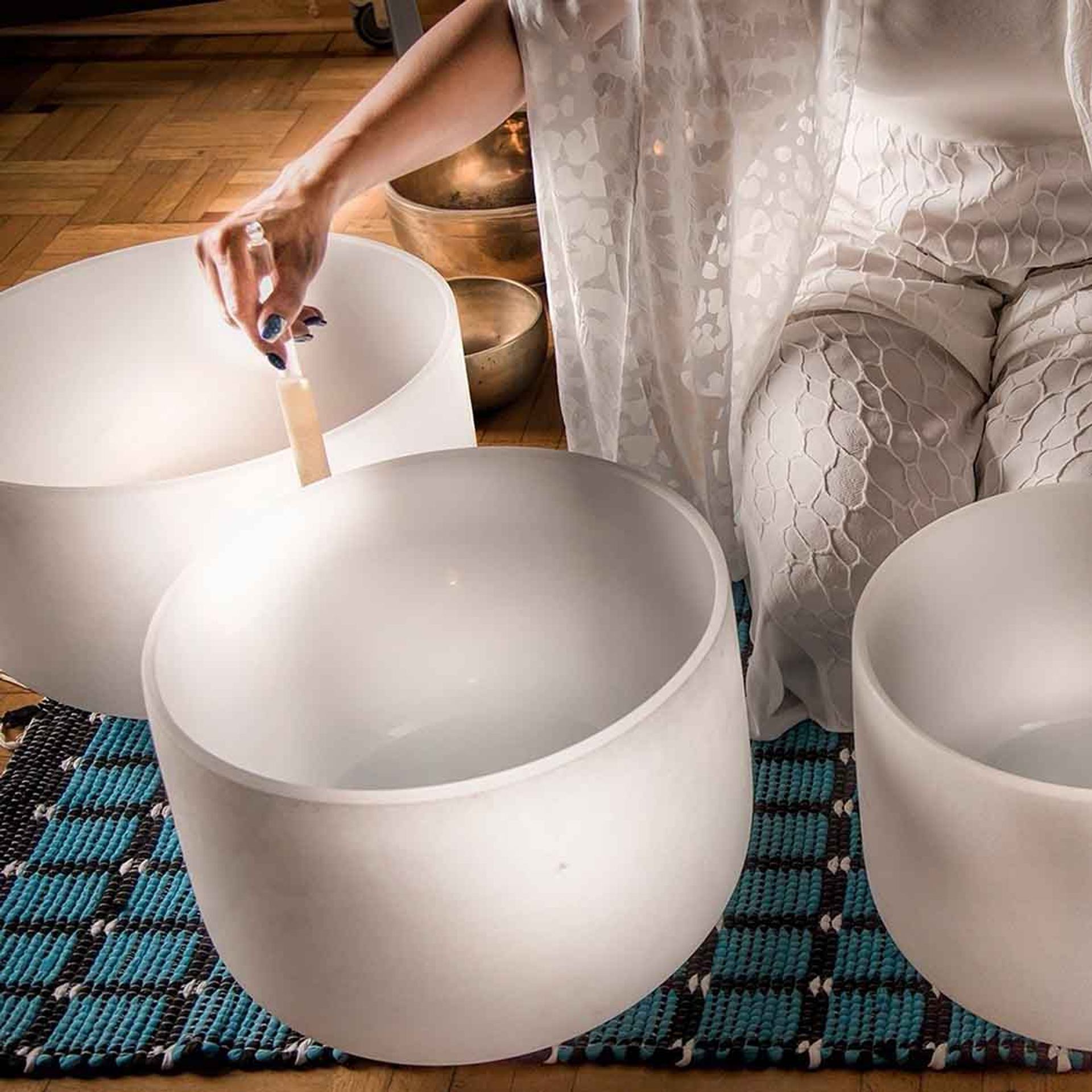 Person in white clothing playing frosted crystal singing bowls on woven blue mat.