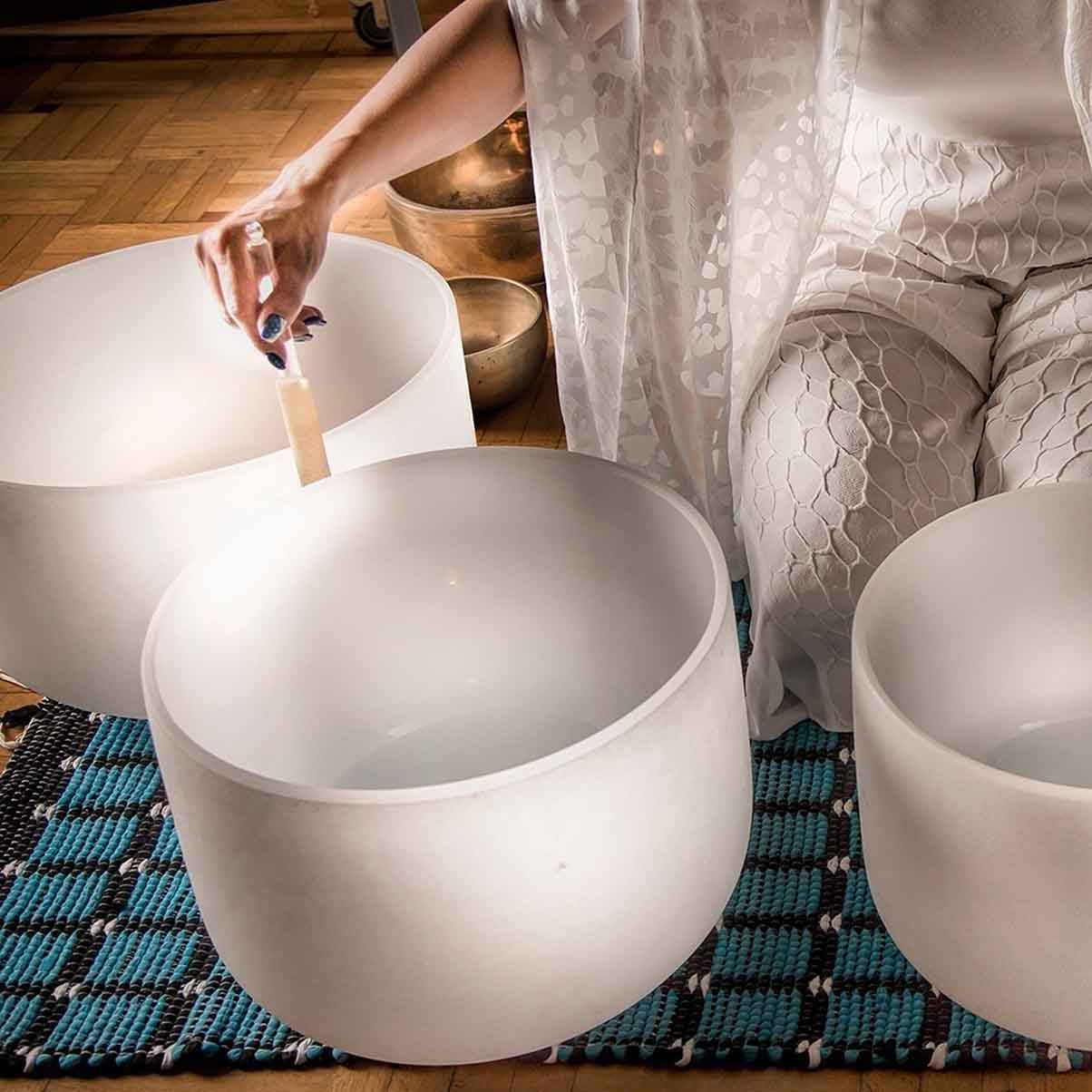 Person in white clothing playing frosted crystal singing bowls on woven blue mat.