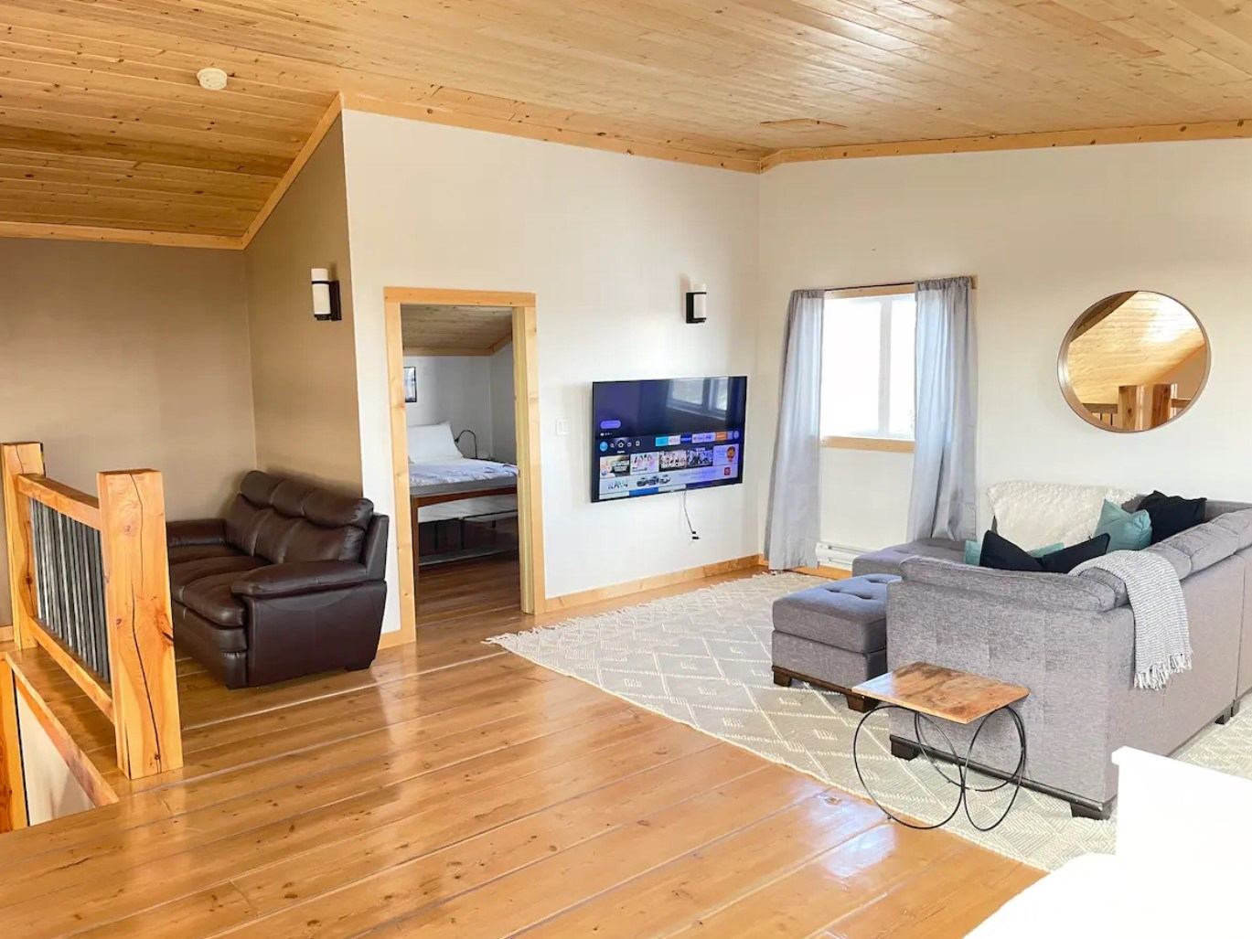 Upstairs lounge with sectional sofa, TV, mirror, and view into bedroom.