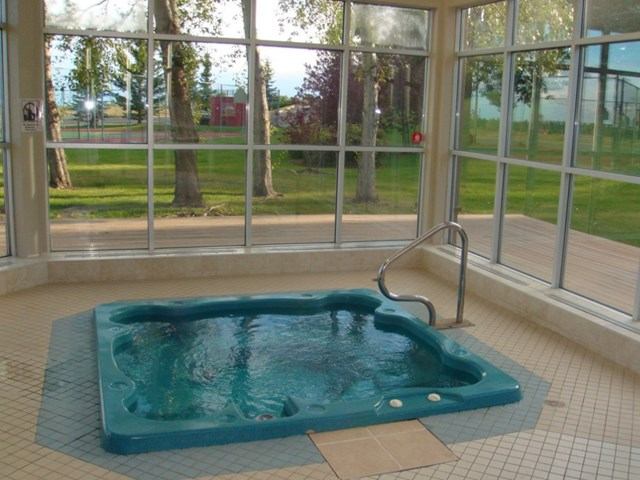 Indoor hot tub in a bright room with large windows overlooking green outdoor space.