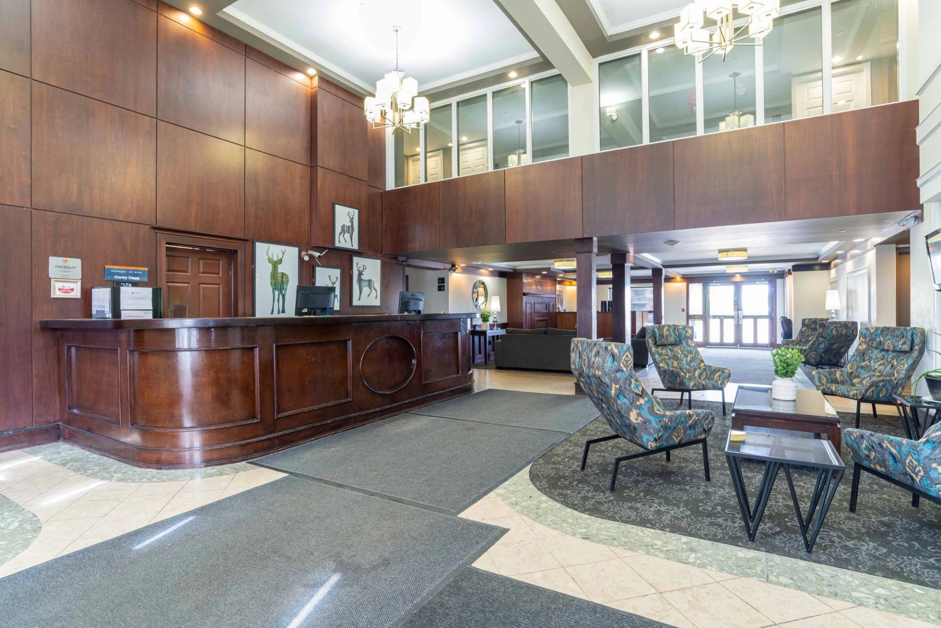 Hotel lobby with wood reception desk, patterned lounge chairs and overhead chandeliers