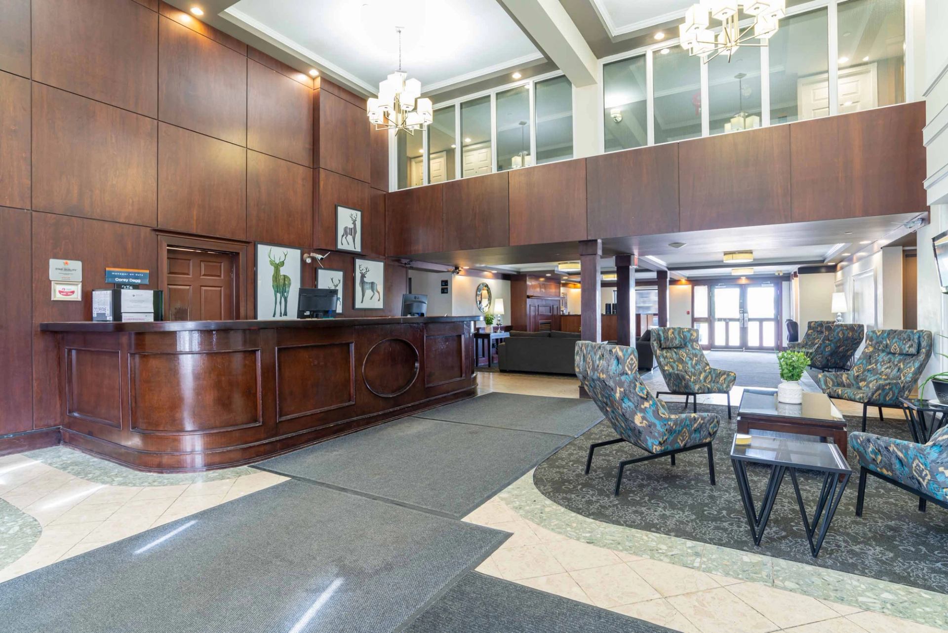 Hotel lobby with wood reception desk, patterned lounge chairs and overhead chandeliers