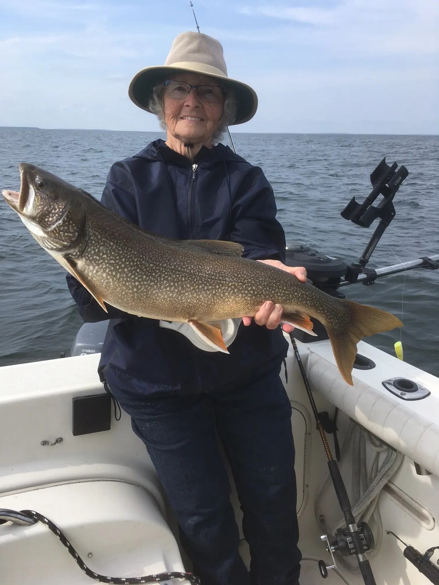 Person on a boat holding a freshly caught large fish over open water.