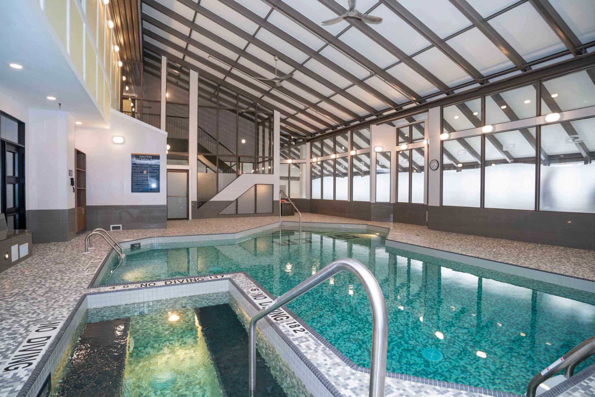 Indoor swimming pool and hot tub area with tiled deck and large windows.
