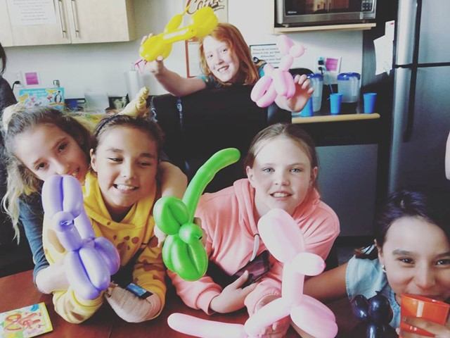 Children smile and hold colourful balloon animals during a library program.