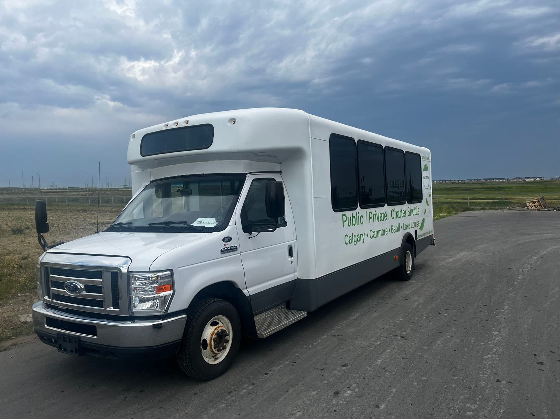 White charter shuttle bus parked on a rural road beneath dark clouds.