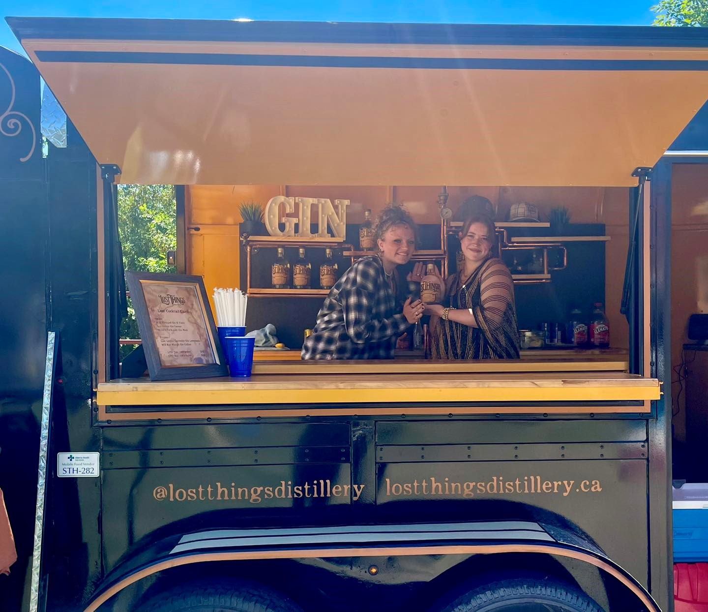 Two women pose for a photo from inside a mobile bar cart.