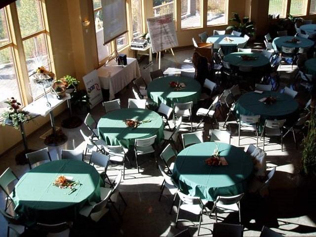 Room with round tables in green cloths, each with chairs and a small centerpiece.