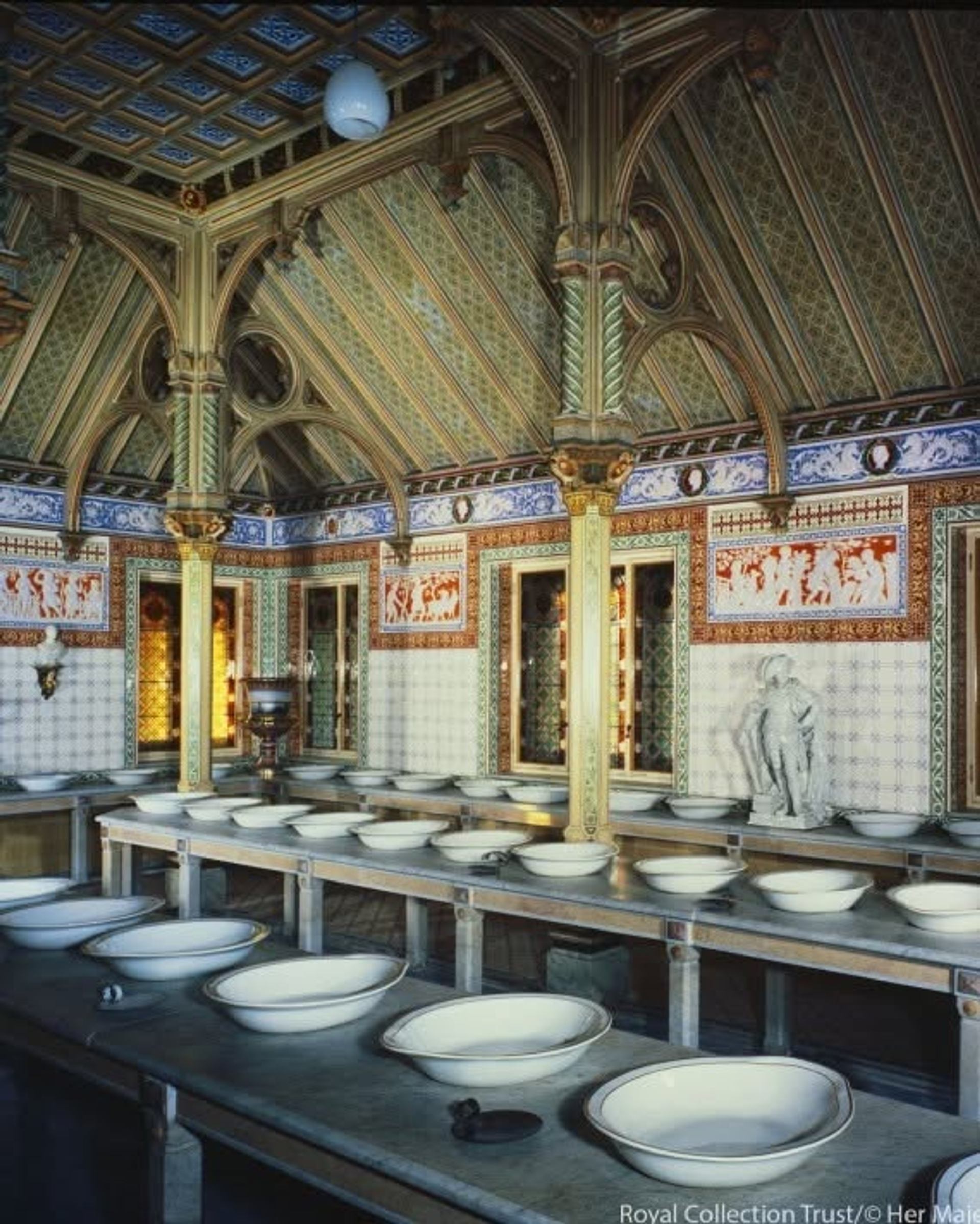 An ornate historic interior display showcases decorative architecture, detailed craftsmanship, and rows of wash basins.
