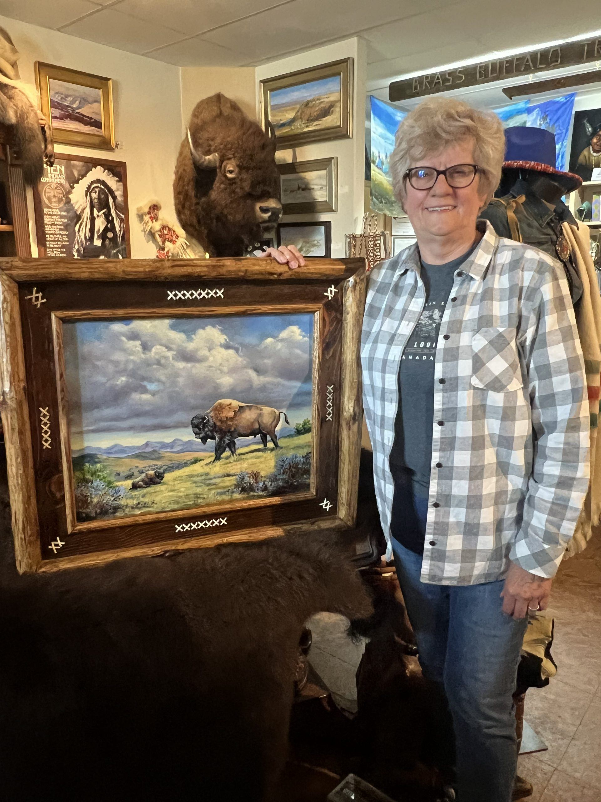 Person standing beside framed bison painting in gallery with taxidermy and artwork.