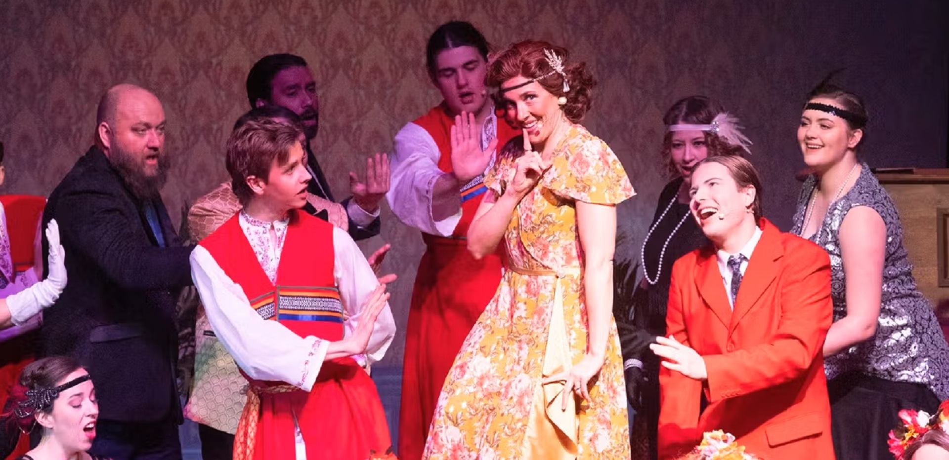 Performers in colorful costumes on stage during a lively theatrical scene.