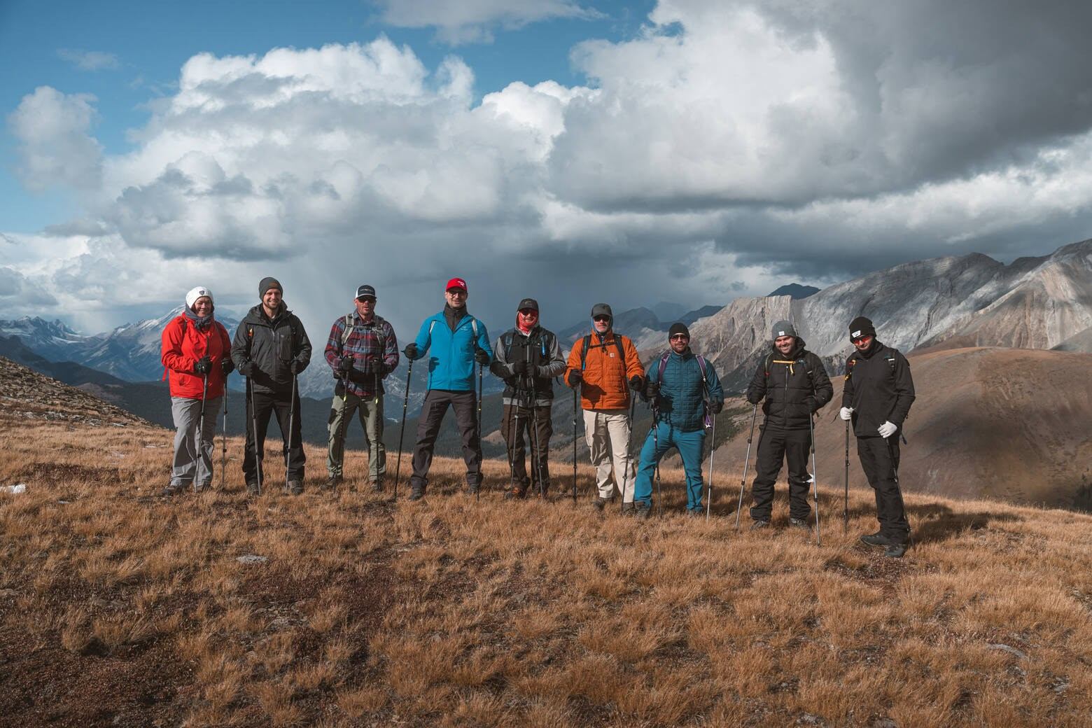 Hikers on a mountain ridge with cloudy skies and distant peaks.